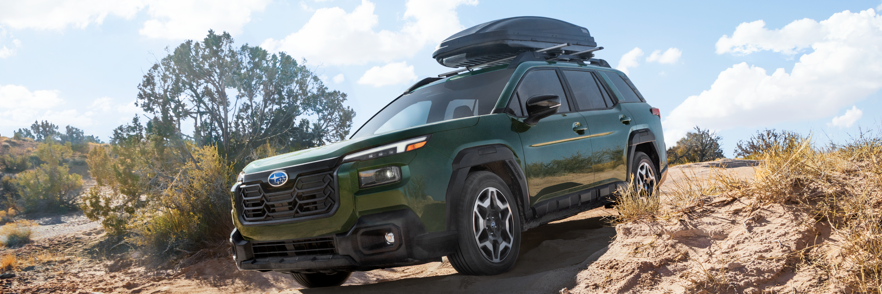 2026 Subaru Outback driving off-road with roof cargo box on a rugged outdoor trail