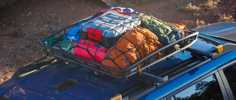 Exterior cargo detail of the 2026 Outback Wilderness in Geyser Blue with optional, accessory and aftermarket equipment, including a Thule roof cargo basket filled with outdoor gear mounted on the cr