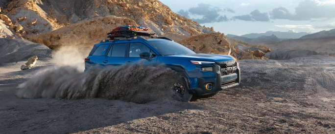 action major of the 2026 Outback Wilderness in Geyser Blue with optional, accessory and aftermarket equipment turning aggressively on a dirt path, kicking up dirt around the vehicle