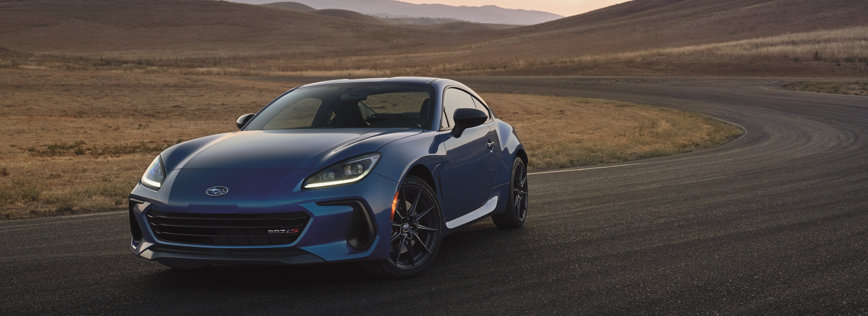Blue Subaru BRZ sports coupe driving on a winding road through an open landscape