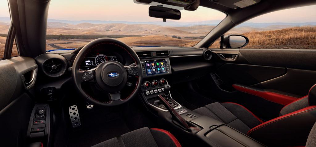 Interior view of a Subaru BRZ showing the driver cockpit, steering wheel, touchscreen display, and manual gear shifter