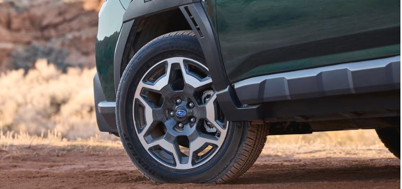 Exterior feature of the tires and wheels on the Outback Touring in Deep Emerald Pearl parked in the dirt.